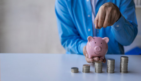 Businessman calculating savings with pile of coins on table, importance of bank and piggy bank to...