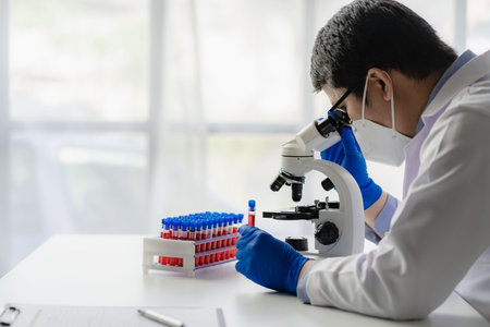 Young asian male doctor checking test report. Science, chemistry, biology. Male scientist holding test tube with red liquid doing test or research in clinical laboratory.の写真素材