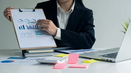 Close up of businesswoman holding pen pointing to paper, business chart for doing math on wooden table, tax, analytical accounting and calculating annual income and expenses, finanの写真素材