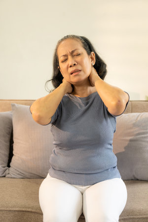 Asian old woman with white hair neck and shoulder pain and sickness on sofa alone at homeの写真素材