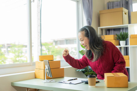 Successful old businesswoman smiling happily receiving new buzzer Asian woman owns a small business online with shipping boxes. concept of working at homeの写真素材