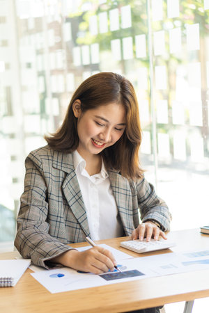 Young woman working on laptop in office, Asian female accountant sitting at her workplace, beautiful freelancer girl working online at home with financial documents. vertical imageの写真素材