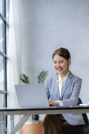 Young woman working on laptop in office, Asian female accountant sitting at her workplace, beautiful freelancer girl working online at home with financial documents. vertical imageの写真素材
