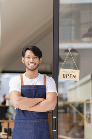 Black male shopkeeper wearing apron with open sign A waitress stands at the entrance to the cafe and food. Successful startup and new store conceptの写真素材