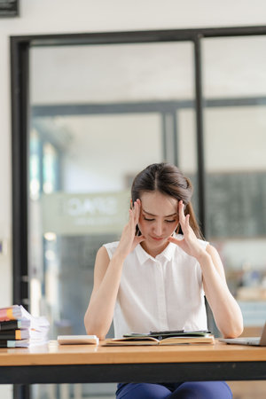 Thinking Asian businesswoman looking at financial statements and making marketing plan using computer on her desk in office holding report papers girl reading financial informationの写真素材