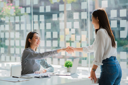 Asian business women shake hands to congratulate success At a meeting of business partners at the table in the officeの写真素材