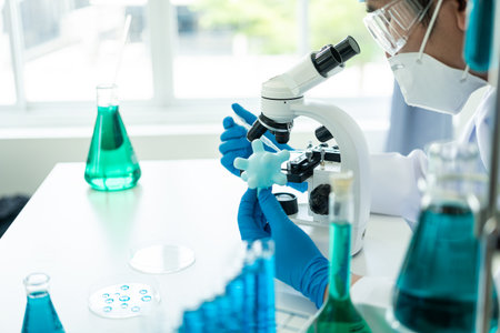 A gloved scientist pours blue acid into a test tube with clear liquid. Scientific research in the chemical industry The doctor examines the analysis in a test tube with a microscopの写真素材