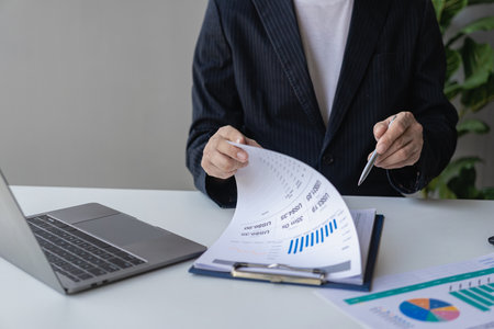Young financial market analyst working at office with laptop while sitting at wooden table Businessman analyzing documents on his desk close up picturesの写真素材