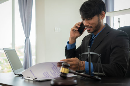 African male lawyer working in law firm justice fights justice Law or judge working with law books, hammer and scales Hammer case report on table in modern officeの写真素材
