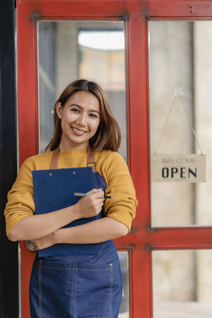 Asian woman standing by the open sign in front of the cafe doorの写真素材