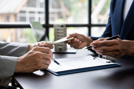 The real estate agent discusses the terms of the home purchase agreement and asks the client to sign paperwork to contract and deliver the home.の写真素材
