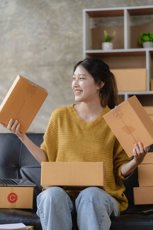 Asian female home-based SME business preparing parcel delivery boxes for online shopping Beginners start small business owners at home. Ordered online with a yellow parcel box. verの写真素材