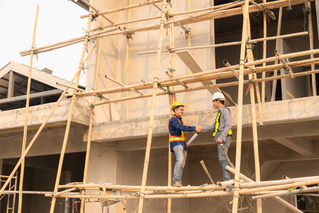 Two Asian male engineers shaking hands and working together Hope stands on the architectural...