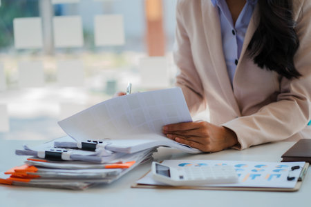 Female accountant analyzing charts, graphs, computer, investment tablet and pressing calculator button above document. Accountants, accountants, clerks, bank consultants and auditoの写真素材