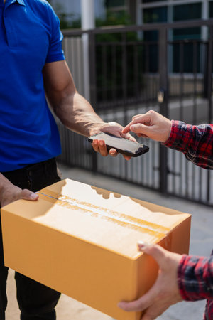 Smiling african american courier holding cardboard box delivering parcel to business customer signing electronic signature POD device on smartphoneの写真素材
