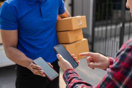 Smiling african american courier holding cardboard box delivering parcel to business customer signing electronic signature POD device on smartphoneの写真素材