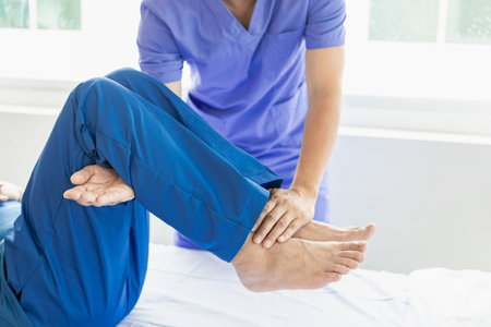 Physiotherapist treating patient at hospital Knee pain in male patient, physiotherapy concept Man stretching his foot with a band while doing physiotherapy at clinicの写真素材