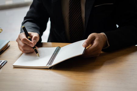 Close-up of businessman's hands writing something down in a notebook and working on his desk.の写真素材