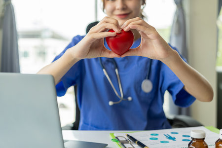 Female doctor holding heart shaped red ball explaining to patient online on laptop computer Concept of cardiology, health services, medicalの写真素材
