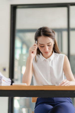 Contemplative Asian female executive in shirt working with laptop in modern office Take notes and come up with a professional plan. Project management Consider financial business cの写真素材