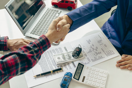 Close-up of a salesperson shaking hands with a man in the sales office after the successful signing of the contract and payment. A car dealer or sales manager offers to sell a car.の写真素材