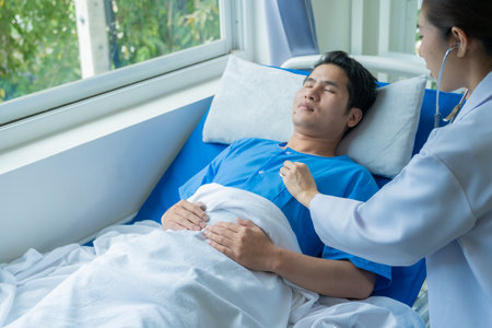 Asian male patient lying on bed with team of doctors providing consultation and relief next to medical health concept.の写真素材