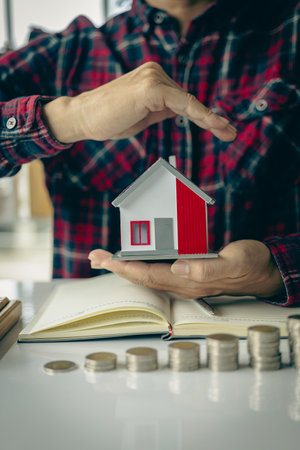 Young man doing house expenses accounting at stack of coins in front, financial investment and saving money for buying a house, financial home loan conceptの写真素材