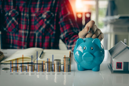 Young man doing house expenses accounting at stack of coins in front, financial investment and saving money for buying a house, financial home loan conceptの写真素材