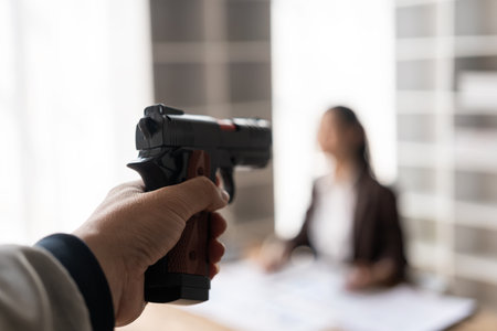 The assailant pointed a handgun at a young female accountant sitting at a desk. Concept of crime and...