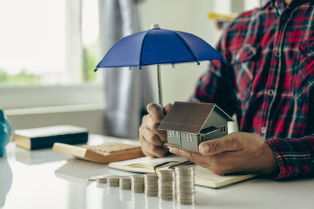Man holding a blue umbrella and a house Insurance agent holds blue umbrella over modern house model Property insurance Home insurance concept Close-up picturesの写真素材
