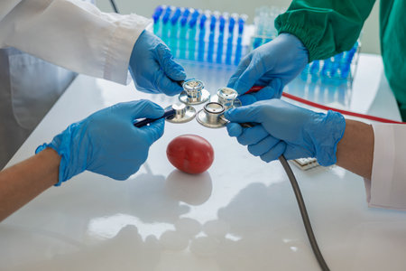 Medical team using stethoscope to examine red heart ball model on table, concept of annual health...
