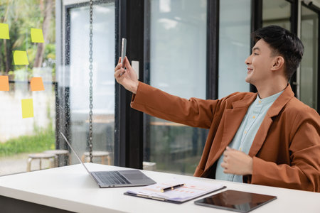 Young Asian businessman in a casual suit uses a computer notebook and talks on the phone to communicate with customers. online business online meetingの写真素材