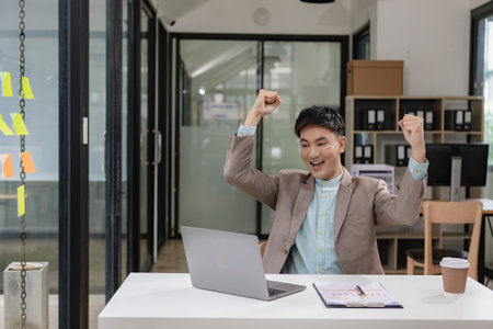 A businessman wearing a formal suit is at work. He sat in front of his laptop computer, raised his...