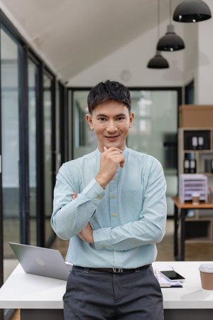 Young Asian businessman in his office and smiling with crossed arms. Young Asian businessman, successful professional, millennial, leader standing with arms crossed in front of comの写真素材