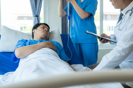 An Asian male patient lies in a hospital bed and is carefully looked after by a doctor. Doctor giving advice to male patient Working on health disease diagnosisの写真素材