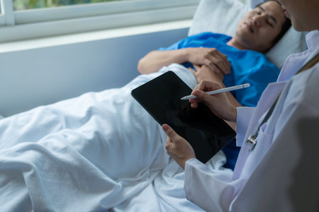 An Asian male patient lies in a hospital bed and is carefully looked after by a doctor. Doctor giving advice to male patient Working on health disease diagnosisの写真素材