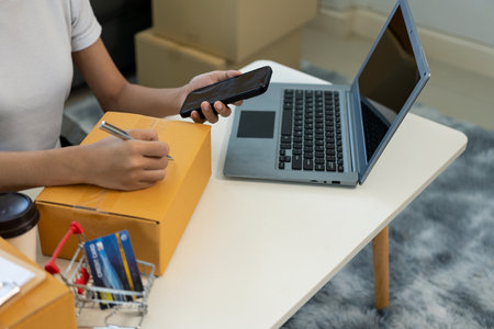 Asian woman working from home SME entrepreneurs use smartphones and laptops for commercial...