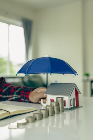 Blue umbrella covering a house model on a wooden table Property insurance, mortgage insurance concept Insurance is risk control in the real estate business.の写真素材