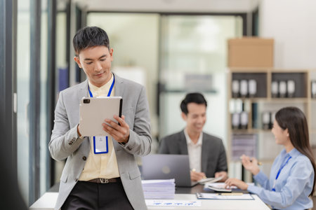 Asian businessman standing in front of a desk in a suit working in a conference room to discuss brainstorming, calculations, joint analysis on company growth goals and gross profitの写真素材