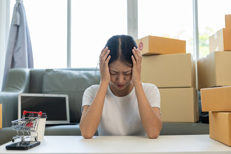 A young Asian entrepreneur feels stressed and worried about declining sales after checking customer orders on his laptop. SME business conceptの写真素材