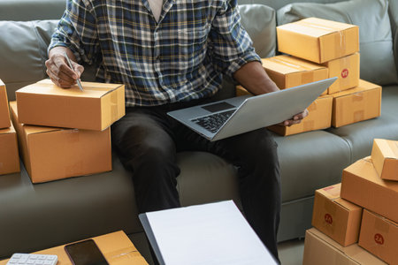 Man working at home office with laptop and parcel box on sofa. Online business and e-commerce concept.の写真素材