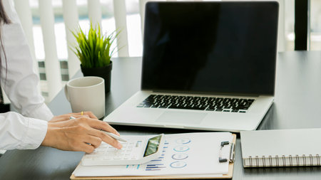 Close-up of businesswoman accountant using calculator and laptop, financial documents to analyze...