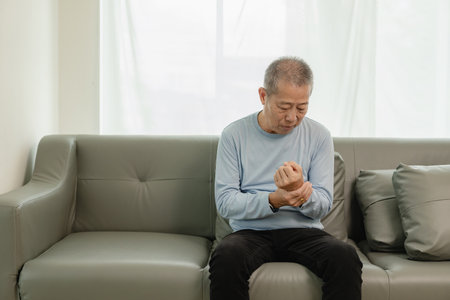 An elderly Asian male patient suffers from pain and numbness in his hand from rheumatoid arthritis. Elderly man massaging hand with pain in wrist health problems conceptの写真素材