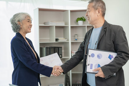 Two senior Asian businessmen, man and woman shaking hands during management meeting and agreement in business partnership concept. Two businessmen shake hands after making a deal.の写真素材