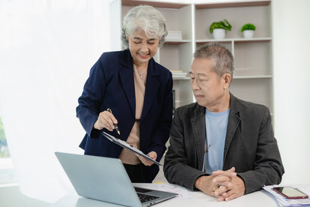 Two senior Asian businessmen, man and woman, work on financial documents to analyze and calculate....
