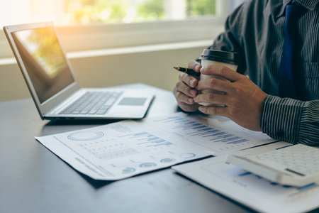 Businessman points at graph charts and uses laptop computer for data analysis, data documents, charts, graphs, reports, market research, development, planning, management, financiaの写真素材