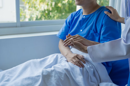 Male patient of Asian descent in bed receives good news from doctor about his recovery in hospital, health, medical and insurance concept.の写真素材
