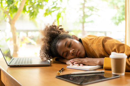 Young african american woman sleeping on the table with laptop and notebookの写真素材