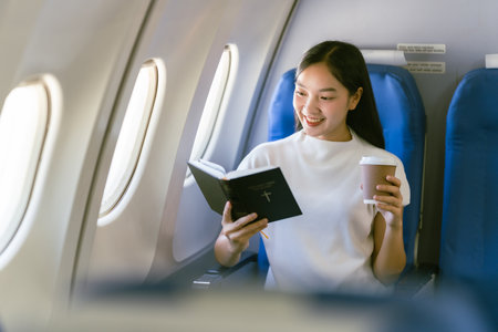 Young woman reading a book in airplane. Travel and tourism concept.の写真素材