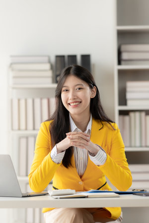 Attractive Asian woman sitting on laptop computer in business office Calculate balances, documents, and check income within the company. vertical pictureの写真素材